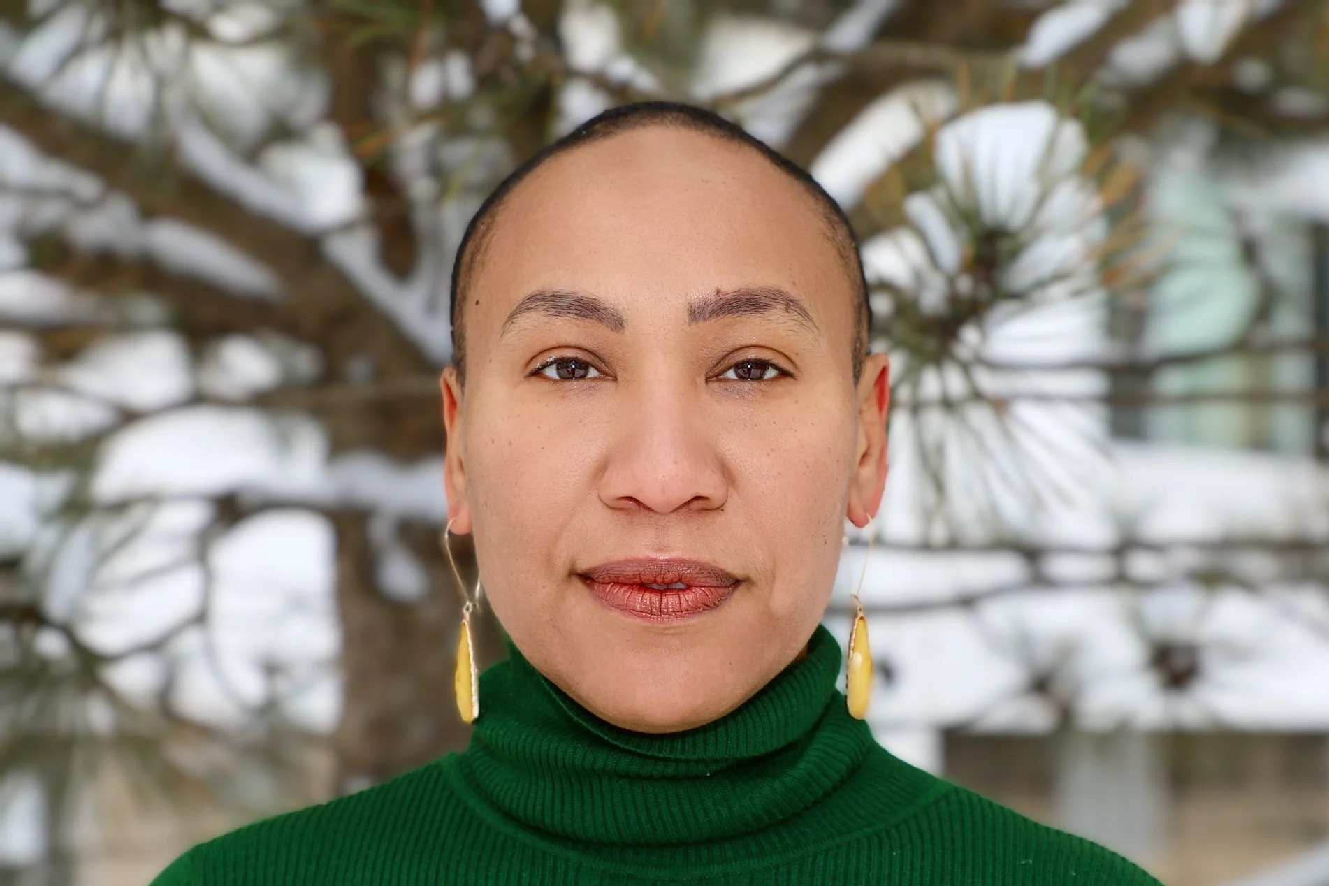 Toni Tavita Martinez outdoors in a Milwaukee winter, snow on the pine behind her, looking directly at the camera.