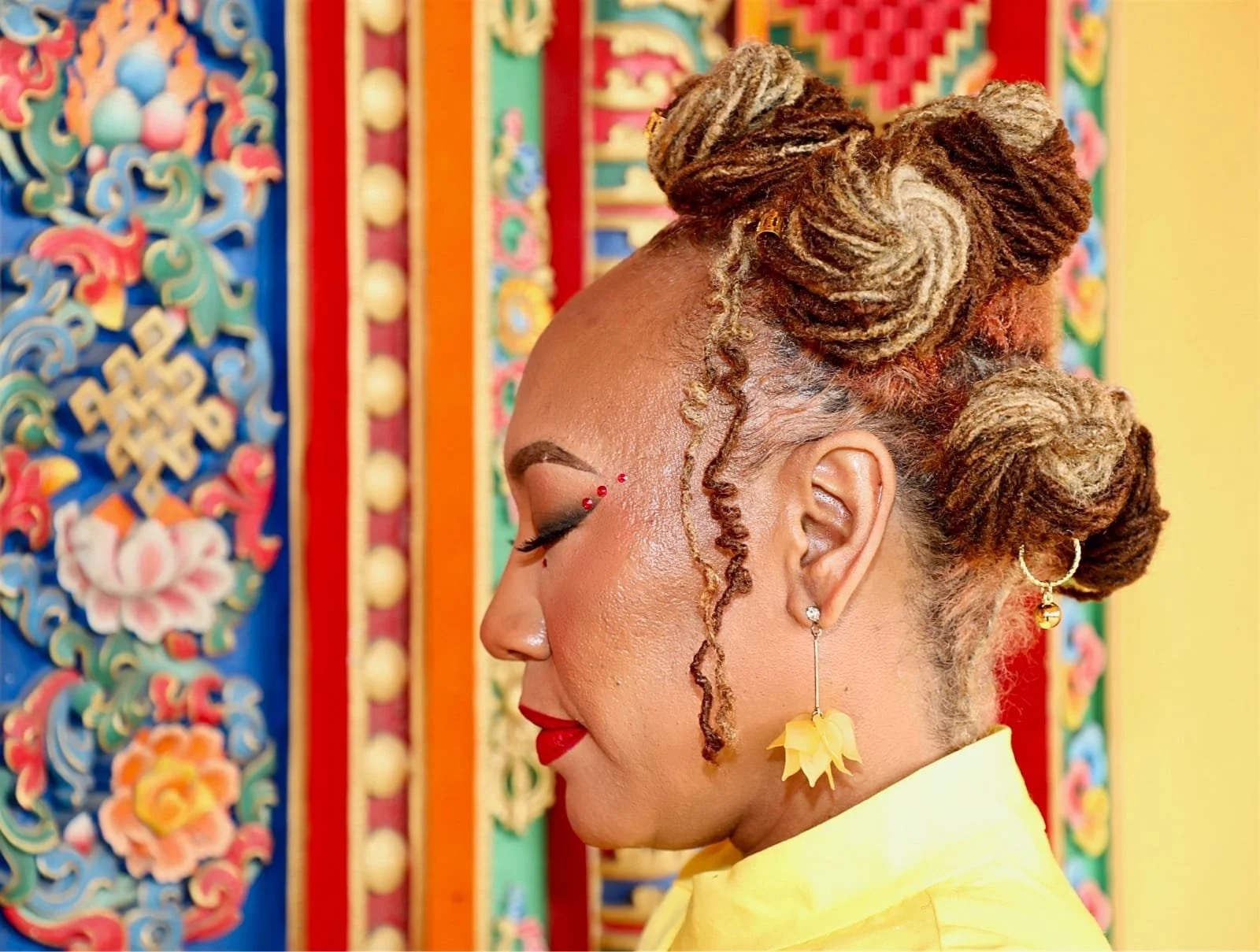 Tavita in profile in a Tibetan temple, against painted panels of lotus, peony and the endless knot.